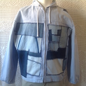 Peut inclure: Une veste en jean bleu clair avec une fermeture éclair et une capuche. La veste est faite de denim patchwork dans différentes nuances de bleu.