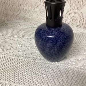 May include: A blue speckled ceramic fragrance lamp with a black top. The lamp has a rounded body and a decorative design. The lamp is likely used for aromatherapy or home fragrance.