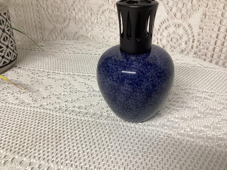 May include: A blue speckled ceramic fragrance lamp with a black top. The lamp has a rounded body and a decorative design. The lamp is likely used for aromatherapy or home fragrance.