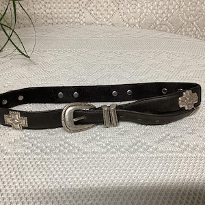 Peut inclure: Une ceinture en cuir noir avec une boucle argentée et des accents décoratifs. La ceinture a un design sud-ouest.
