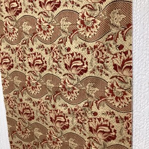 May include: A beige fabric with a repeating pattern of red and beige stylized flowers. The flowers are arranged in a wavy pattern.