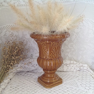 Puede incluir: Una urna de cerámica marrón con un patrón decorativo de hojas. La urna está llena de hierba de la pampa seca.