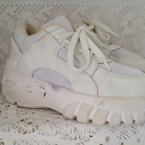 Peut inclure: Des baskets blanches à plateforme avec une semelle épaisse et des lacets blancs. Les chaussures ont une empeigne en mesh et en cuir.