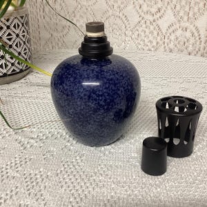 May include: A navy blue speckled ceramic oil lamp with a black top and a black metal decorative sleeve. A small black cap sits next to the lamp. The lamp is a decorative home decor item.