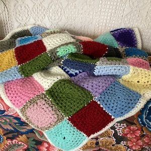 Peut inclure: Une couverture en patchwork crochetée avec des carrés de différentes couleurs, notamment rose, rouge, vert, bleu, jaune et blanc.