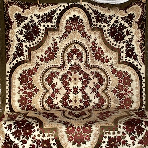 Può includere: Una coperta vintage con un motivo floreale in tonalità di rosso, verde e crema. La coperta ha un bordo a frangia ed è realizzata in un tessuto morbido e vellutato.