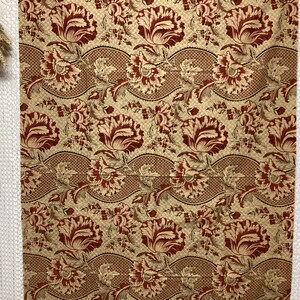 May include: A fabric swatch with a repeating pattern of red and cream floral designs on a beige background.