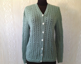 Pode incluir: Um cardigan de malha verde claro com decote em V e fecho de botões. O cardigan tem um padrão de renda delicado.