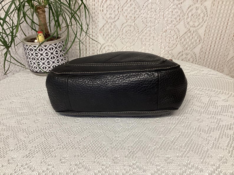 Pu&ograve; includere: Borsa in pelle nera con finitura strutturata e cuciture bianche. La borsa ha una forma arrotondata e una cerniera superiore. Il fondo della borsa &egrave; visibile, mostrando la pelle strutturata e le cuciture.