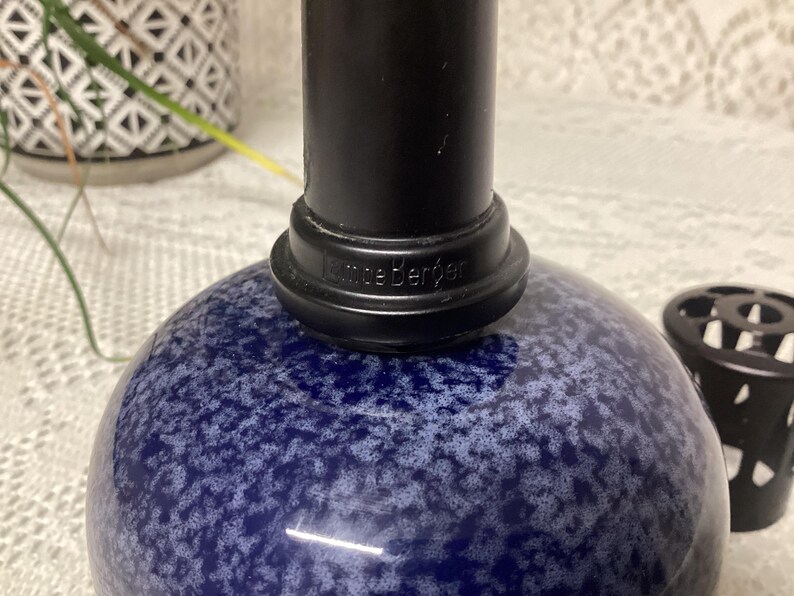 May include: A close-up of a blue and white speckled glass object with a black cylindrical top. The base of the top has the word "Kneeb&euml;rger" printed on it. A black decorative object is in the background.