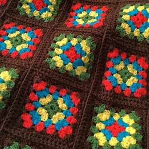 Peut inclure: Une couverture en crochet marron avec des carrés colorés. Les carrés sont faits de fil rouge, jaune, bleu et vert.