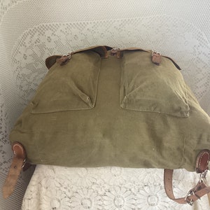 May include: A vintage green canvas backpack with leather straps and buckles. The backpack has two large pockets on the front.