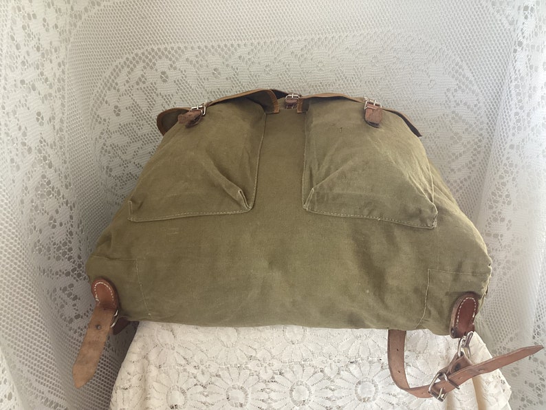 May include: A vintage green canvas backpack with leather straps and buckles. The backpack has two large pockets on the front.