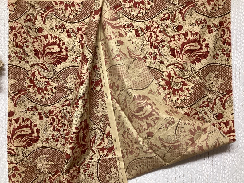 May include: A beige fabric with a repeating pattern of red and gold floral designs. The fabric has a subtle texture and a slightly distressed look.