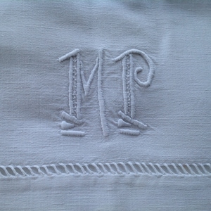 May include: White linen fabric with a stitched monogram of the letters "MP" in a cursive font.