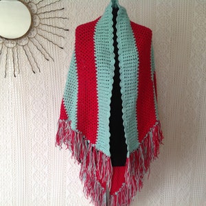 May include: A crocheted shawl with red and light blue stripes and fringe. The shawl is displayed on a mannequin.