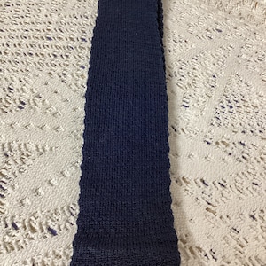 Puede incluir: Una bufanda de punto azul oscuro. La bufanda está hecha de un material suave y texturizado.