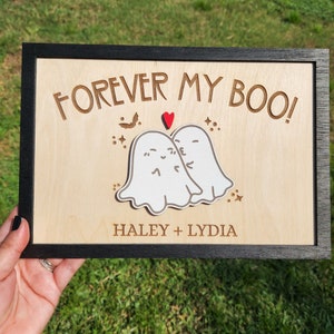 May include: A wooden sign with the text "Forever My Boo!" and two white ghosts kissing. The sign also includes a red heart and the names "Haley + Lydia".