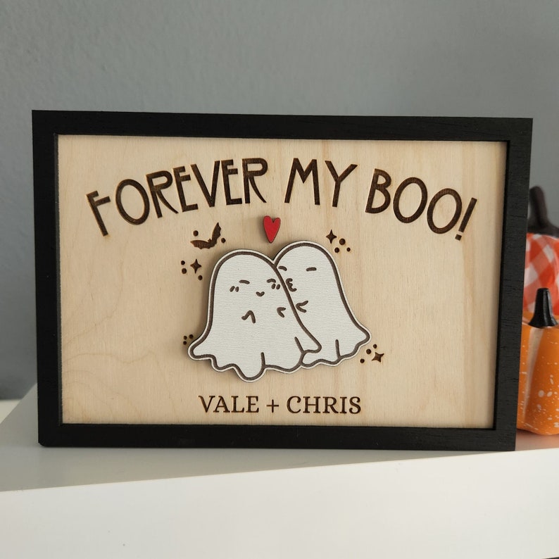May include: A wooden sign with the text "FOREVER MY BOO!" and two ghosts with hearts. The sign is framed in black and has the names "VALE + CHRIS" at the bottom.