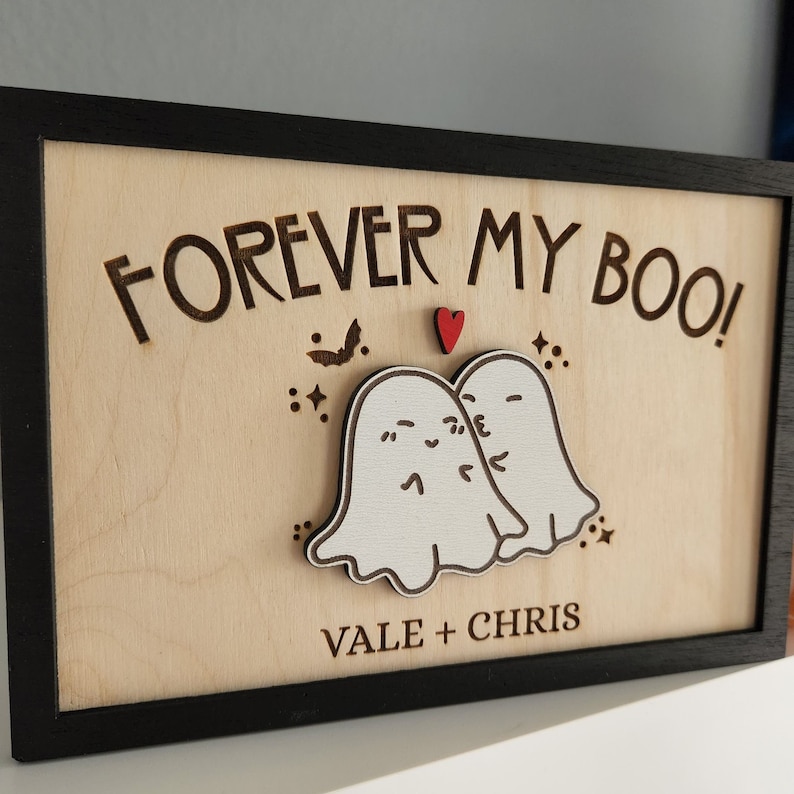 May include: A wooden sign with a black frame and the text "FOREVER MY BOO!" in a decorative font. Two white ghosts are kissing with a red heart above them. The text "VALE + CHRIS" is below the ghosts.