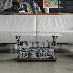 Könnte beinhalten: Ein weißes Ledersofa mit einem Glastisch aus einem wiederverwendeten Automotorblock. Der Tisch hat eine Holzbasis.