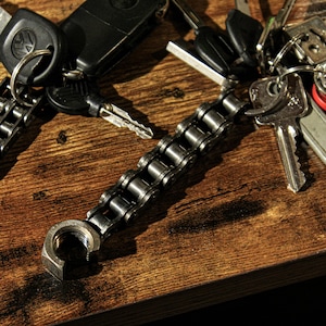May include: A silver chain keychain with a car key, a house key, and a variety of other keys. The keychain is made of a thick, durable chain and has a large, round loop at the end. The keys are all silver and have different shapes and sizes.