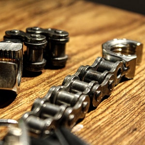 May include: A silver metal chain with a silver metal clasp. The chain is made of individual links that are connected together. The clasp is a simple design with a hook and a loop.