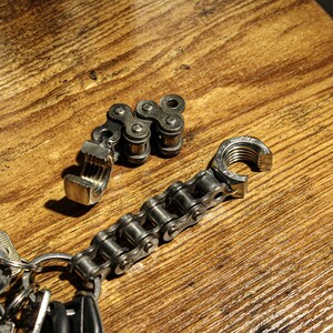 May include: A silver chain keychain with a bottle opener and a clamp attached. The keychain is on a wooden surface.