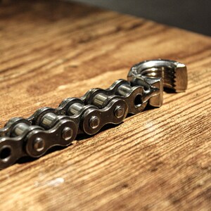 May include: A silver chain with a metal clasp. The chain is made of individual links and is lying on a wooden surface.