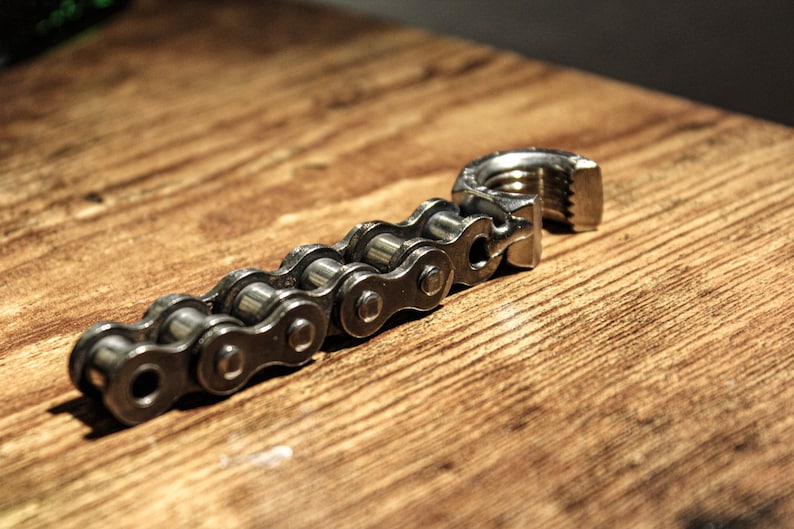 May include: A silver chain with a metal clasp. The chain is made of individual links and is lying on a wooden surface.