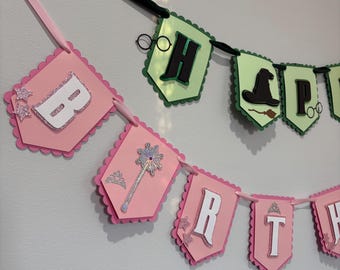 May include: Pink and green banner with letters and themed images. The top banner has the letters "H" and "A" with a witch hat and glasses. The bottom banner has the letters "B", "R", and "T" with a wand, crown, and stars.
