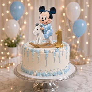 Peut inclure: Un gâteau rond blanc décoré de glaçage bleu clair et blanc, surmonté d'une figurine de Mickey Mouse sur un cheval à bascule blanc et d'une bougie chiffre un dorée. Le gâteau est posé sur un présentoir à gâteau en argent.