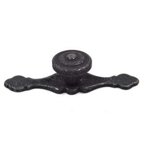Op de afbeelding: Zwarte metalen kastknop met een decoratief, sierlijk ontwerp. De knop heeft een ronde, platte bovenkant en een lange, smalle basis.