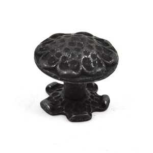 Puede incluir: Pomo de armario de metal negro con un dise&ntilde;o floral decorativo. El pomo tiene una parte superior redonda y una base en forma de estrella.