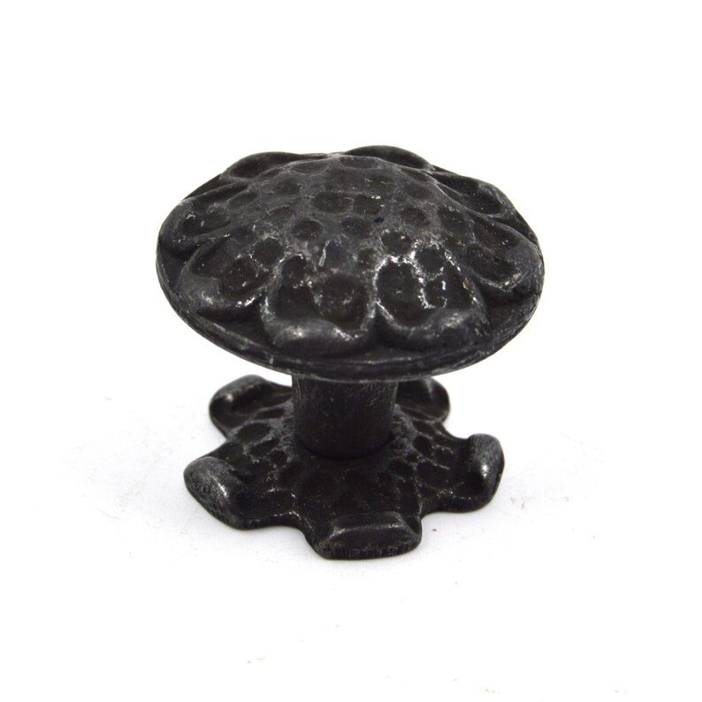 Puede incluir: Pomo de armario de metal negro con un dise&ntilde;o floral decorativo. El pomo tiene una parte superior redonda y una base en forma de estrella.