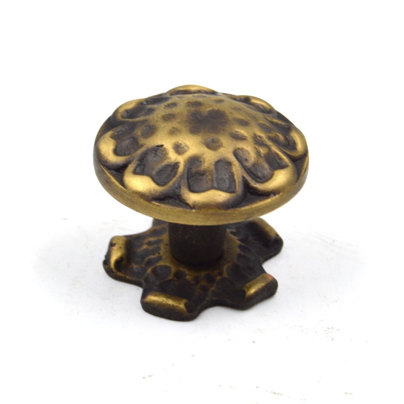 Puede incluir: Un pomo de armario de metal dorado con un dise&ntilde;o floral decorativo. El pomo tiene una base en forma de estrella.