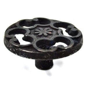 以下が含まれることがあります： 装飾的な花のデザインが施された黒い鋳鉄製のキャビネットノブ。ノブは丸いベースと短いステムを持っています。