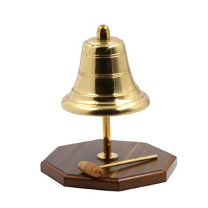 May include: A gold-coloured brass bell with a wooden base and a wooden mallet. The bell is mounted on a wooden stand with a round base.