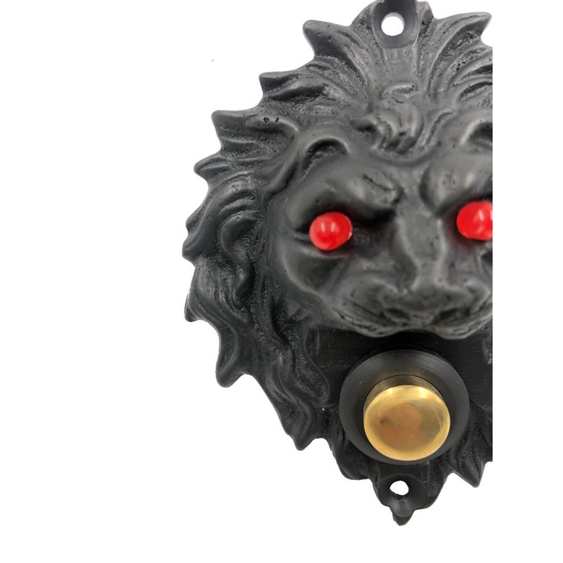 May include: Black lion head door knocker with a brass button and red glowing eyes.
