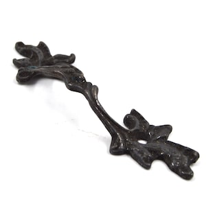May include: A black metal decorative pull with a floral design. The pull has a smooth, slightly curved surface and is designed to be attached to a drawer or cabinet door.