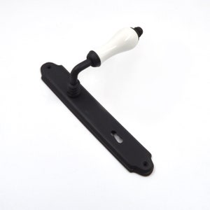 May include: Black door handle with a white ceramic lever. The handle has a keyhole and a decorative backplate.