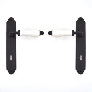 May include: A pair of black door handles with white ceramic levers. The handles have a traditional design and are suitable for interior doors.