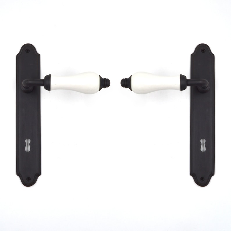 May include: A pair of black door handles with white ceramic levers. The handles have a traditional design and are suitable for interior doors.