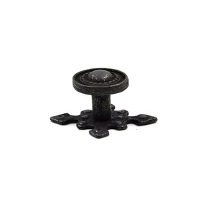 May include: Black metal cabinet knob with a cross-shaped base and a round top with a decorative border.