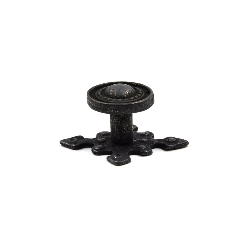 May include: Black metal cabinet knob with a cross-shaped base and a round top with a decorative border.