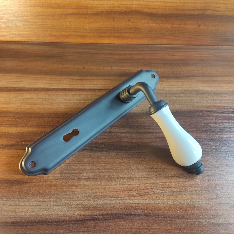 May include: Black door handle with a white ceramic lever. The handle has a keyhole and a decorative design.