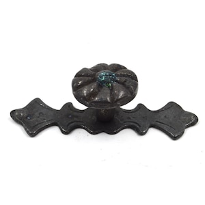 Könnte beinhalten: Schwarzer Metall-Schrankknauf mit dekorativem Blumenmuster und türkisfarbenem Zentrum.