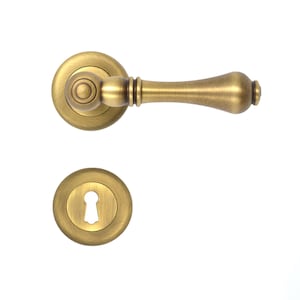 Puede incluir: Una manilla de puerta dorada con una roseta redonda decorativa y una palanca larga y curva. La manilla tiene una cerradura para una llave tradicional.