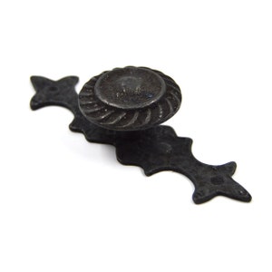 May include: Black metal cabinet door pull with a decorative, ornate design. The pull has a round knob with a rope-like pattern.