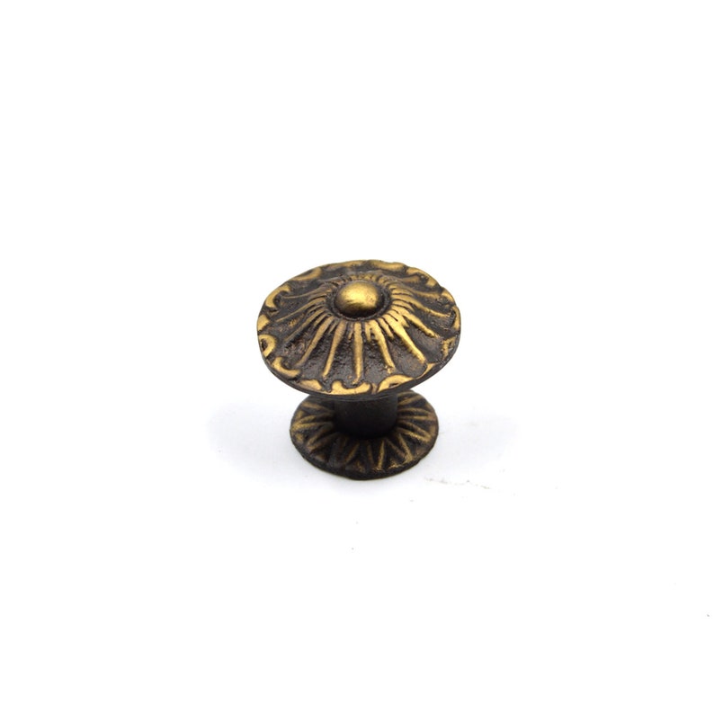 May include: A decorative brass cabinet knob with a circular design and a raised center. The knob has a dark brown finish.